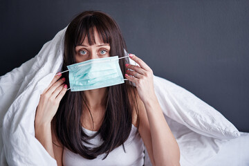 Young woman wearing face protection mask sittig on bed has fever by virus.