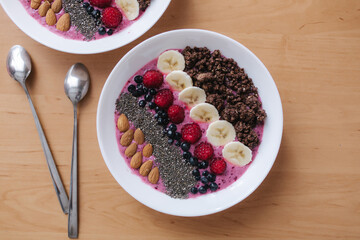 Smoothie bowl with fresh raspberry, blueberry, chia seeds, almonds, banana, and chocolate flakes. Morning breakfast on wooden table. Top view of two plates. vegan food