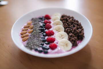 Smoothie bowl with fresh raspberry, blueberry, chia seeds, almonds, banana, and chocolate flakes. Morning breakfast on wooden table