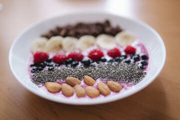 Smoothie bowl with fresh raspberry, blueberry, chia seeds, almonds, banana, and chocolate flakes. Morning breakfast on wooden table