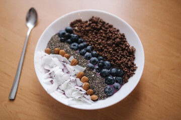 Fresh smoothie bowl with blueberry, chia seeds, almonds, coconut flakes and chocolate flakes. Morning breakfast on wooden table. Lactose free yogurt