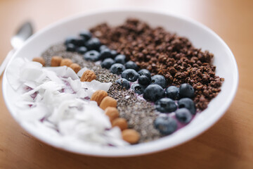 Fresh smoothie bowl with blueberry, chia seeds, almonds, coconut flakes and chocolate flakes. Morning breakfast on wooden table. Lactose free yogurt