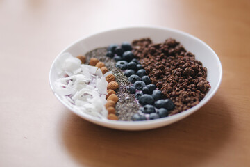 Fresh smoothie bowl with blueberry, chia seeds, almonds, coconut flakes and chocolate flakes. Morning breakfast on wooden table. Lactose free yogurt