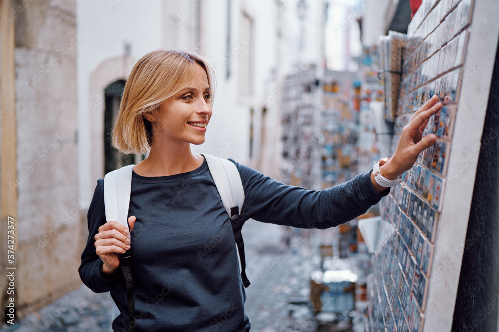 Wall mural Travel and shopping. Young traveling woman with backpacks choose magnets in souvenir shop in Portugal.