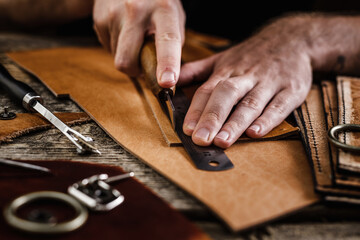 Close up of a shoemaker or artisan worker hands. Leather craft tools on old wood table. Leather craft workshop.