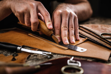 Close up of a shoemaker or artisan worker hands. Leather craft tools on old wood table. Leather craft workshop. - obrazy, fototapety, plakaty
