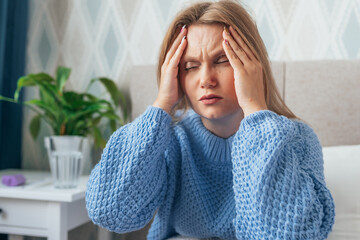 Beautiful blonde young woman having a strong headache sitting in bed. Female holding head with her...