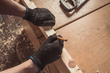 Close-up The man measures a wooden board with a ruler and marks with pencil the necessary points...