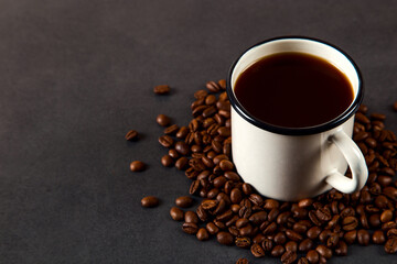 Black delicious coffee in an iron mug and scattered grains on a stone table. Authentic drink, copy space.