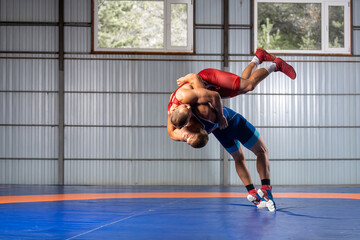 Two men in sports wrestling tights and wrestling during a traditional Greco-Roman wrestling in fight on a wrestling mat. Wrestler throws his opponent’s chest through