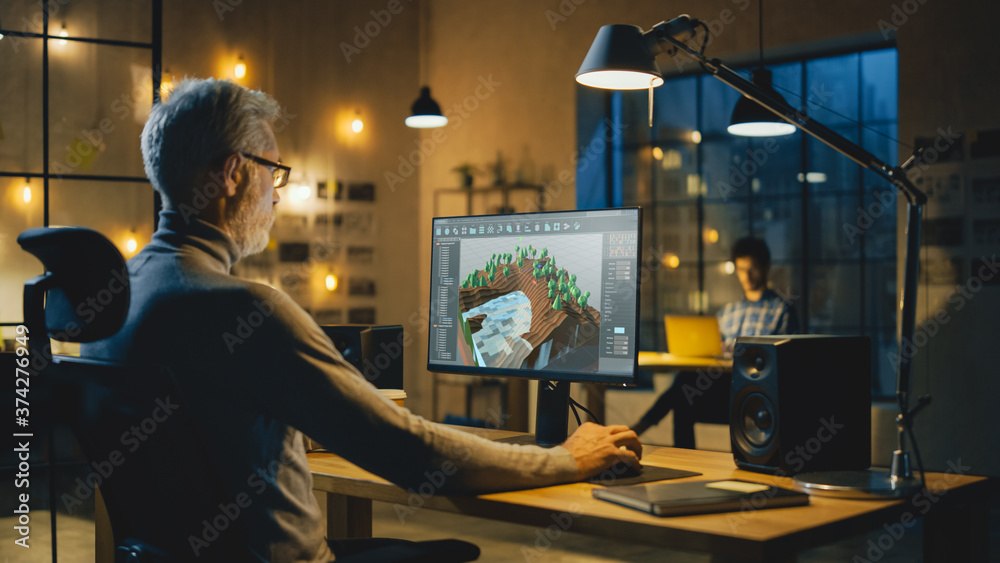 Poster In the Evening Creative Middle Aged Video Game Developer Works on a Desktop Computer with Screen 3D Videogame Level Design. Professional Office Employee Working Late in the Evening in His Studio 