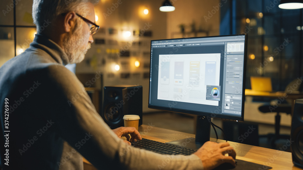 Poster Creative Middle Aged Mobile Software Designer Sitting at His Desk Uses Desktop Computer with Screen Showing Smartphone Application Design Process. Stylish Modern Studio Office