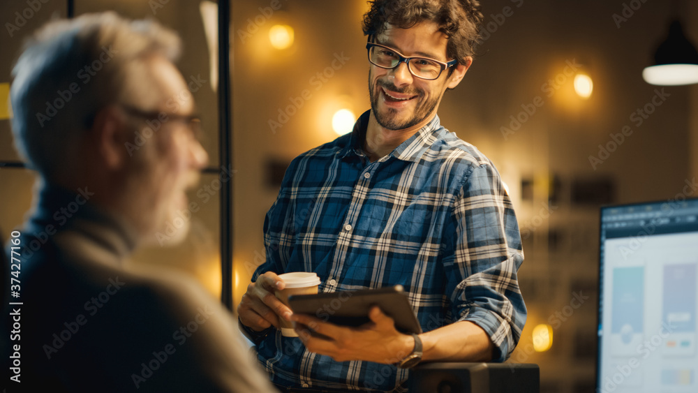 Aufkleber In the Evening Creative Middle Aged Smartphone Software Developer Works on a Desktop Computer with Screen Showing Application Design, Has Conversation with Younger Specialist who Uses Tablet Computer