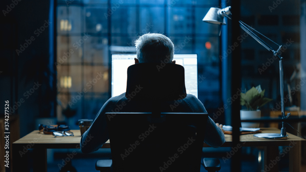 Aufkleber Back view Shot of the Businessman Sitting at His Desk Using Desktop Computer. Stylish Office Studio with Dimmed Light and Big Cityscape Window View