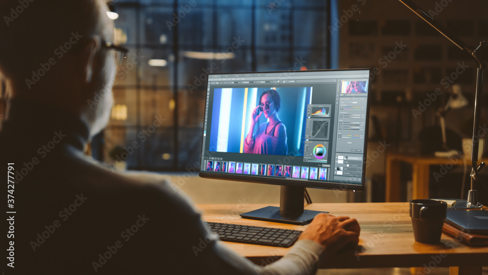 Aufkleber Over the Shoulder: Creative Middle Aged Digital Editor Works in Photo Editing Software on His Personal Computer with Big Display. In the Background Evening in Modern Loft Studio Office