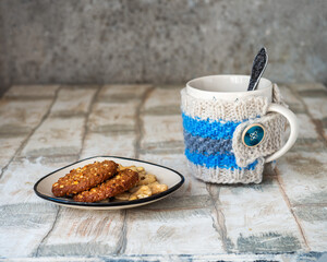 Tea with oatmeal cookies. A large mug in a hand-knitted warmer made of terkh flowers yarn