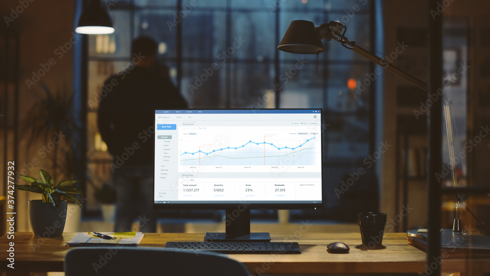 Poster Shot of a Desktop Computer with Statistics Graph, Chart and Various Data, Showing Company Growth and Success. In the Background Businessman Drinks from a Cup Looks at the Night City out of the Window