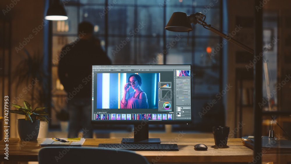 Poster Desktop Computer with Photo Editing Software Standing on the Desk in the Modern Creative Office. In the Background Designer Drinks from a Cup Looks at the Night City out of the Window.