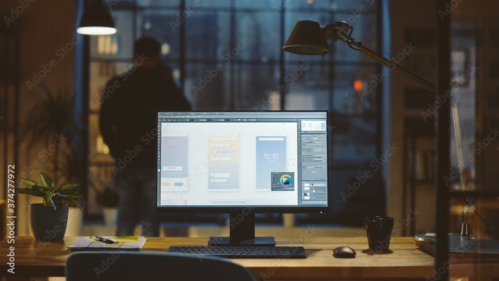 Poster Shot of a Desktop Computer in the Office Shows Screen with Mobile Phone Application Design, Software UI Development. In the Background Designer Drinks from a Cup Looks at the Night City out of Window.