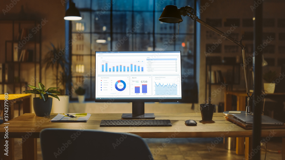 Poster Shot of a Desktop Computer with Statistics Graph, Chart and Various Data, Showing Company Growth and Success. In the Background Warm Evening Lighting and Open Space Studio with City Window View.