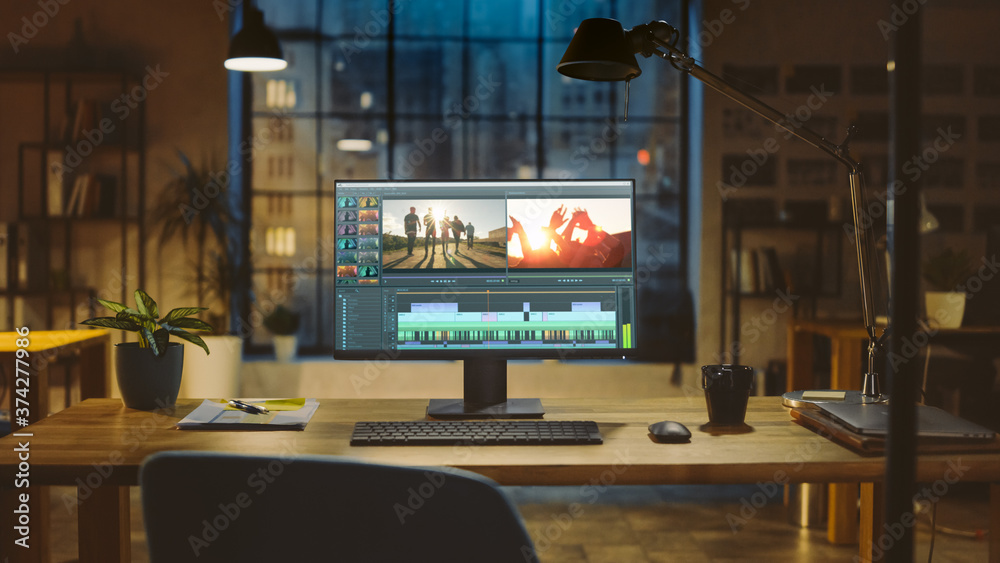 Poster Shot of a Desktop Computer Standing on a Desk with Professional Video Montage Editing Software. In the Background Warm Evening Lighting and Open Space Studio with City Window View.
