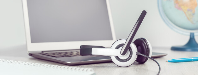 Laptop with blank screen and headphones on white desk grey background world globe. Distant learning or working from home, online courses or travel agent concept. Helpdesk or call center headset banner
