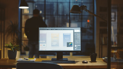 Shot of a Desktop Computer in the Office Shows Screen with Mobile Phone Application Design, Software UI Development. In the Background Designer Drinks from a Cup Looks at the Night City out of Window.