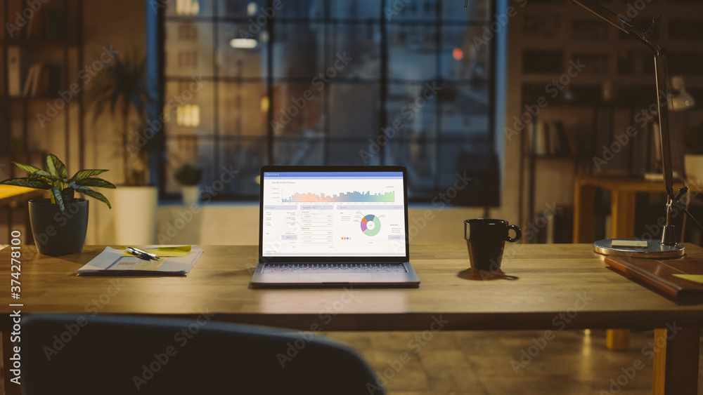Poster Shot of a Laptop on a Desk with Statistics Graph, Chart and Various Data, Showing Company Growth and Success. In the Background Warm Evening Lighting and Open Space Studio with City Window View.