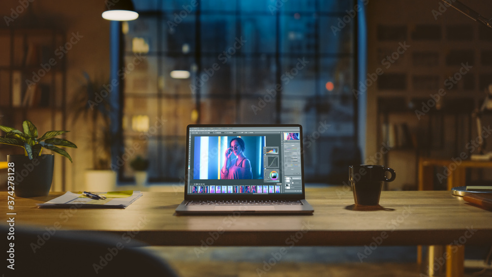 Poster Shot of a Laptop Computer in the Modern Office Showing Photo Editing Software. In the Background Warm Evening Lighting and Open Space Studio with City Window View