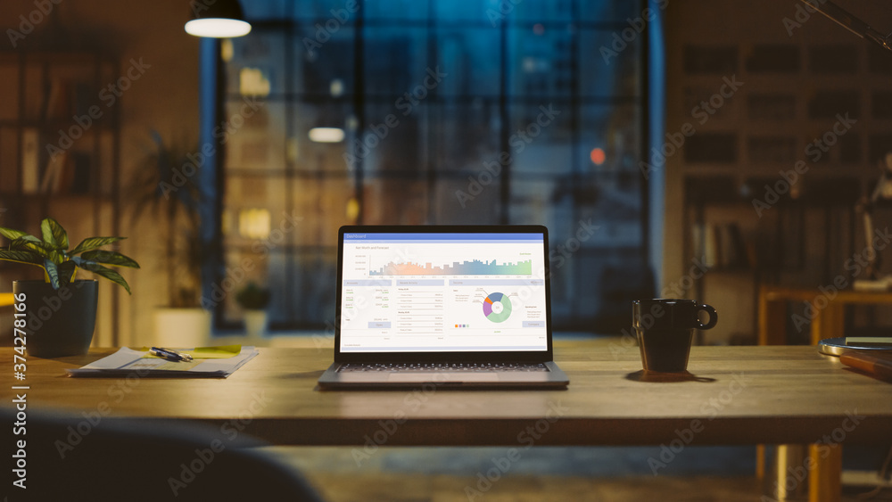Poster Shot of a Laptop on a Desk with Statistics Graph, Chart and Various Data, Showing Company Growth and Success. In the Background Warm Evening Lighting and Open Space Studio with City Window View.