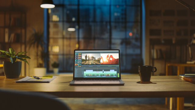 Shot of a Laptop Computer Standing on a Desk with Professional Video Montage Editing Software. In the Background Warm Evening Lighting and Open Space Studio with City Window View.