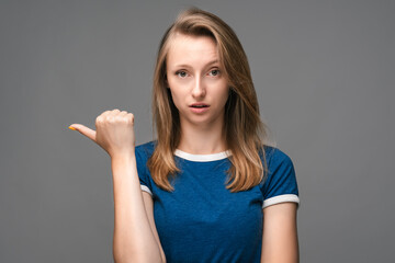 Fototapeta premium Young woman with blonde straight hair over isolated gray background pointing finger to the side. Presenting your product