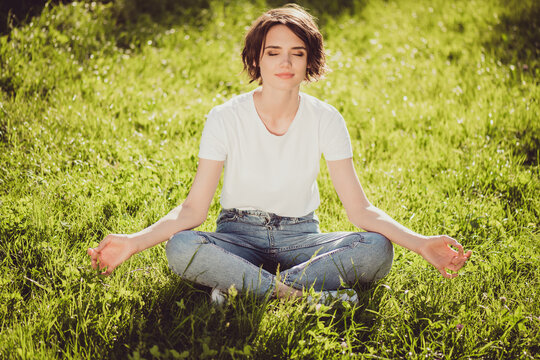 Photo of cute charming lady sitting lend ground fresh green grass enjoy sun rays eyes closed nature harmony morning meditation time rest escape city crowd people colorful park outdoors