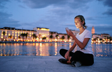 Young woman using smartphone at city evening lights.