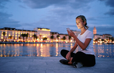 Fototapeta na wymiar Young woman using smartphone at city evening lights.