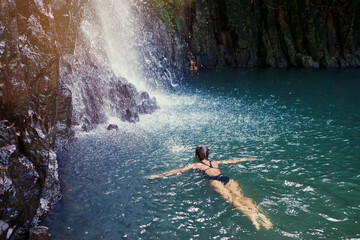 Travel and nature. Young woman swimming in tropical waterfall pool.