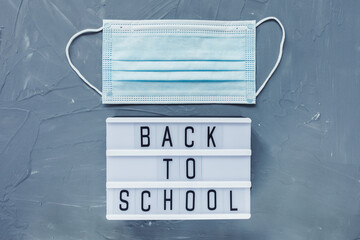 Words BACK TO SCHOOL, and medical disposable mask on gray background. Education or studying during coronavirus COVID-19 concept, flat lay, top view, copy space