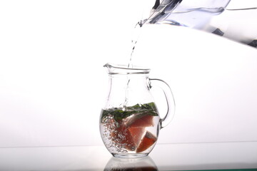 a carafe of water grapefruit and mint stands on a white background