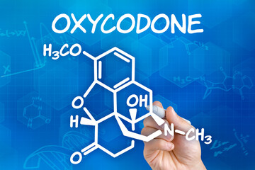 Hand with pen drawing the chemical formula of Oxycodone