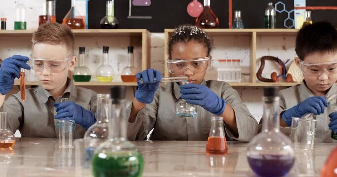 Laboratory experience in a chemistry lesson, kids in protective glasses pours a liquids into a flasks, modern education at school, international school class.