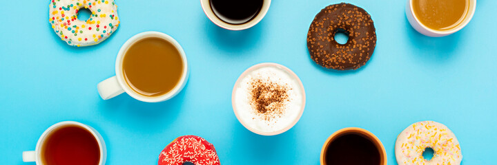 Tasty donuts and cups with hot drinks, coffee, cappuccino, tea on a blue background. Concept of sweets, bakery, pastries, coffee shop, meeting, friends, friendly team. Banner. Flat lay, top view