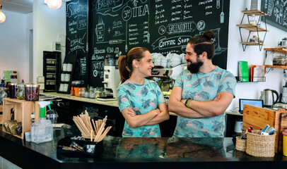 Couple of coffee shop owners posing while looking at each other and smiling