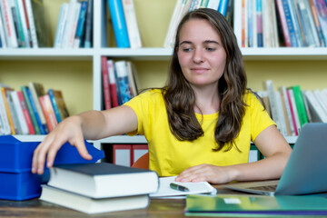 Young german female student learning with book and computer at desk