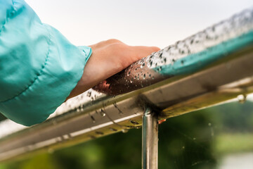 Close-up of a girl's hand in a turquoise jacket on an iron railing with raindrops, top view