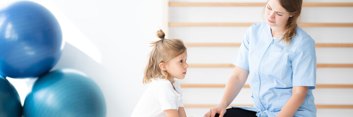 Cute little blond girl exercising with her professional physicia