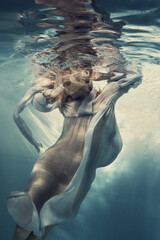 A woman in a blue dress, thin and developing as in weightlessness, floats under water.