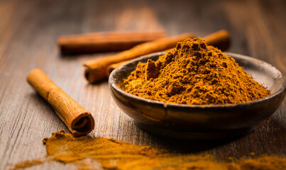 Cinnamon powder in wooden bowl with cinnamon sticks