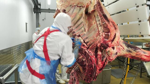 Butcher in uniform cutting hanging meat with knife