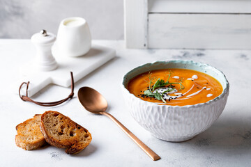 Vegetarian autumn pumpkin and carrot soup with cream, black cumin seeds and green pea micro greens. Fall and winter comfort, healthy slow food