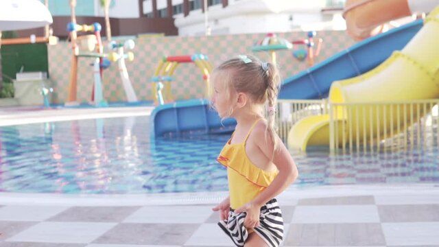 A little girl in a swimsuit walks in a deserted water park in the summer.